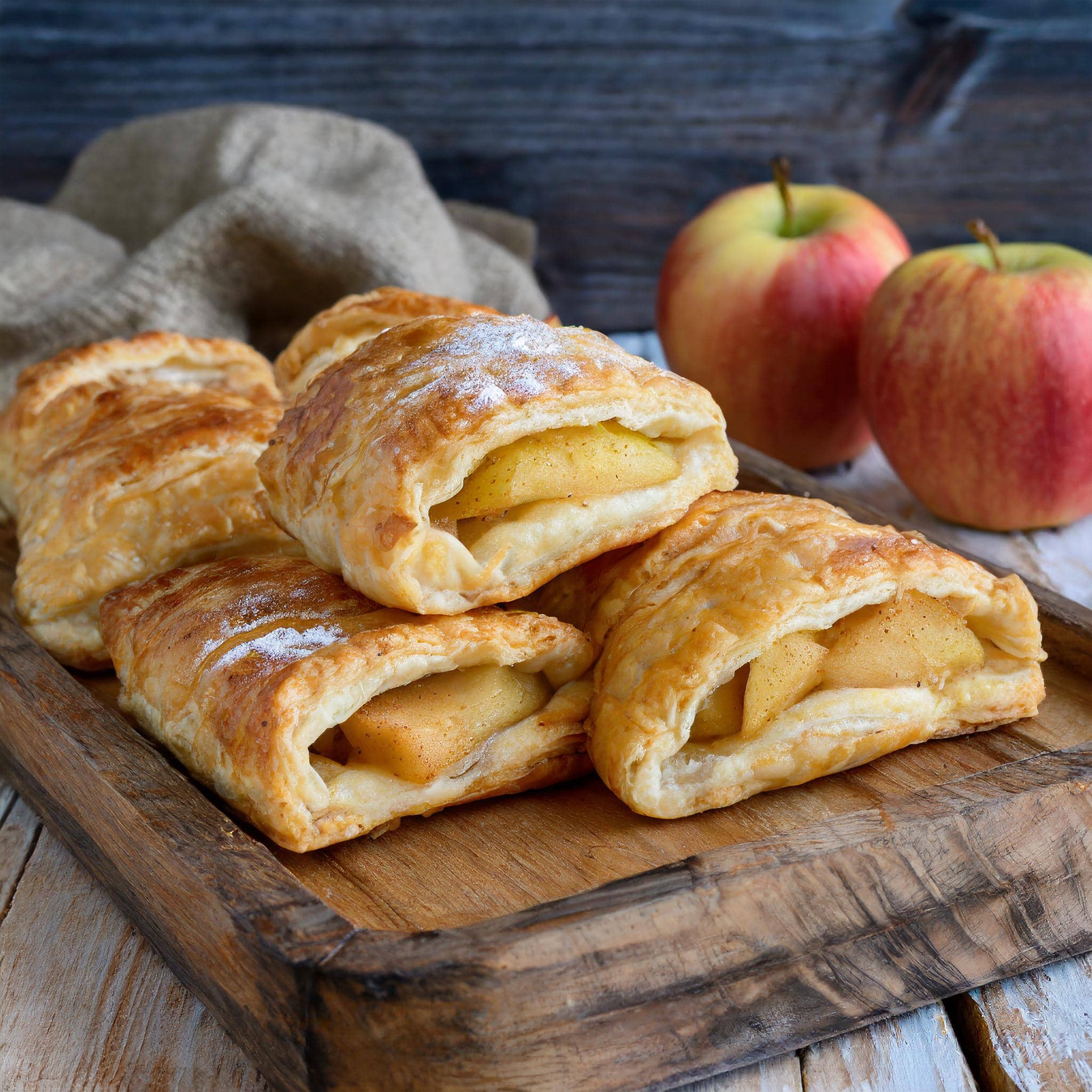 Freshly baked apple turnovers on a wooden tray.